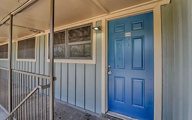 Exterior view of an apartment entrance with a blue door and light gray siding.