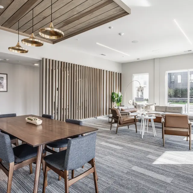 Modern Communal Living Room A modern communal living space featuring a dining table with gray chairs, cozy seating area with brown chairs, and a bright atmosphere with large windows and greenery.