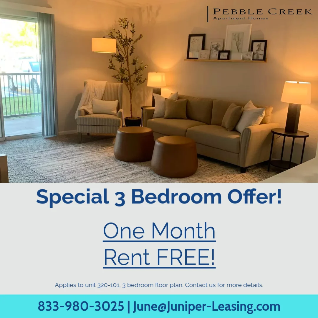 Interior view of a spacious living room in an apartment, featuring beige furniture, large windows, and a decorative plant.