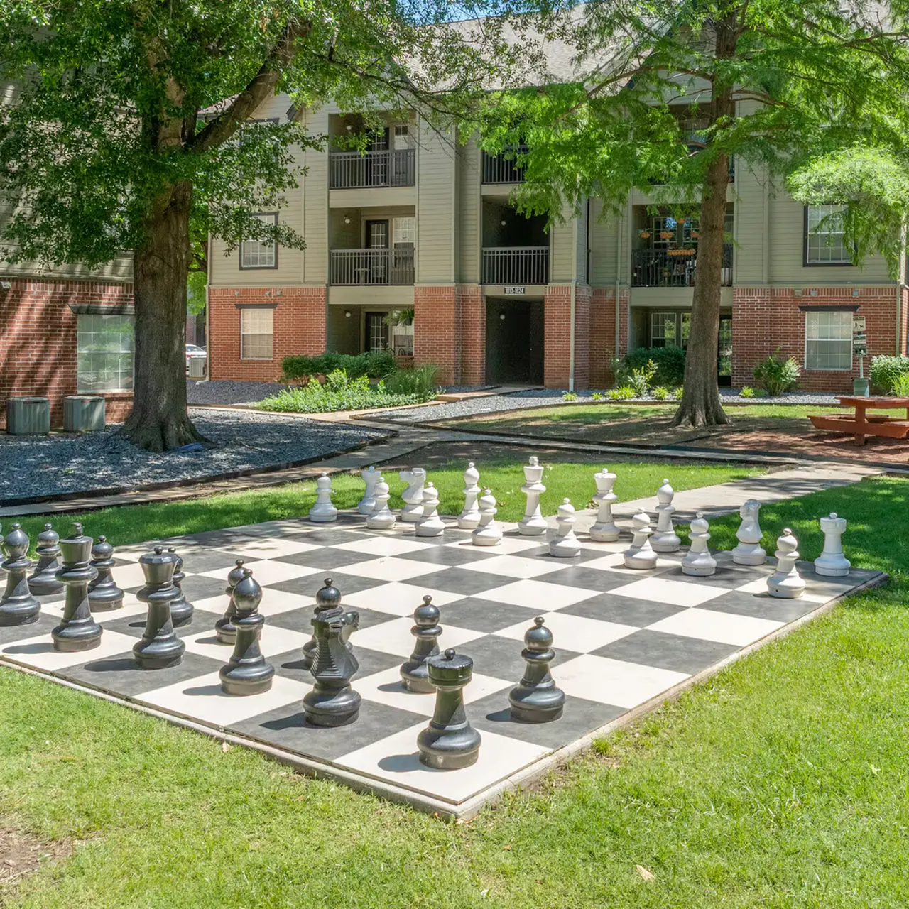 Outdoor Chess Set in Apartment Complex A large outdoor chess set situated on a grassy area in an apartment complex, surrounded by trees and buildings.