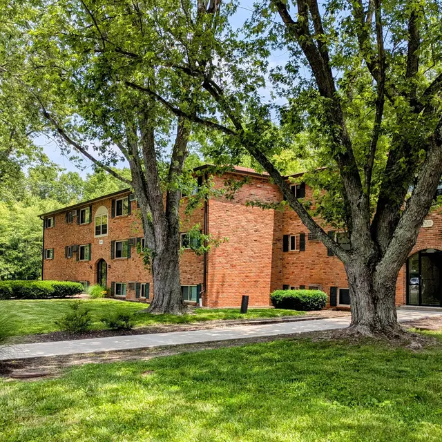 Exterior view of a brick apartment building surrounded by trees and lush grass.