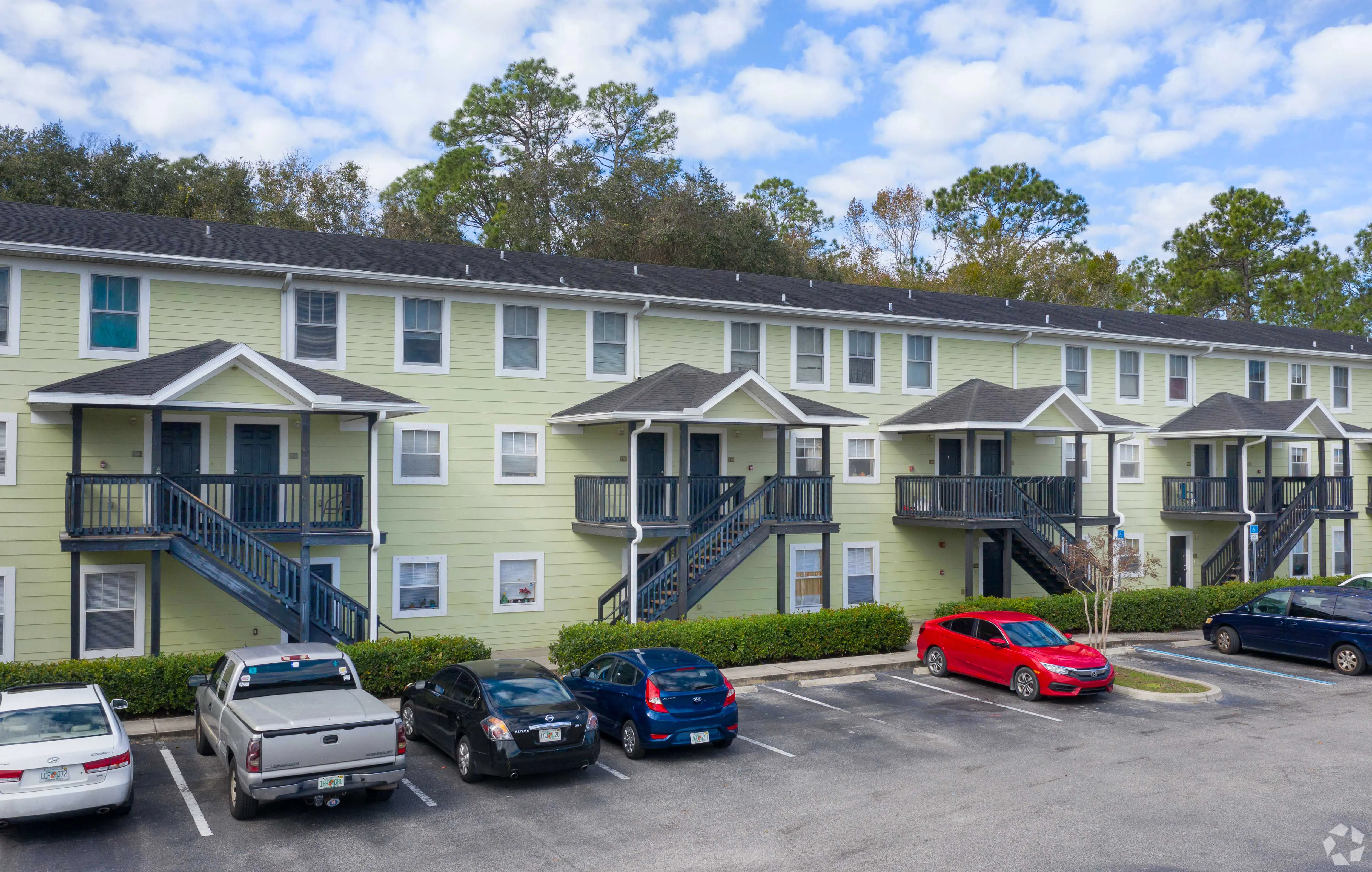 Multi-Story Apartment Complex A multi-story apartment complex with a light green exterior, featuring balconies and staircases. Several parked cars are visible in front.