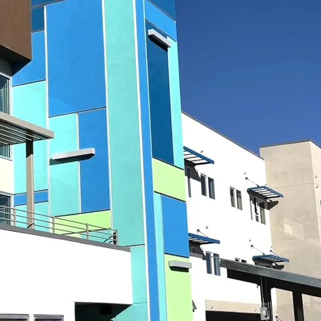 A vibrant building facade featuring a mix of blue, green, and beige colors under a clear blue sky.