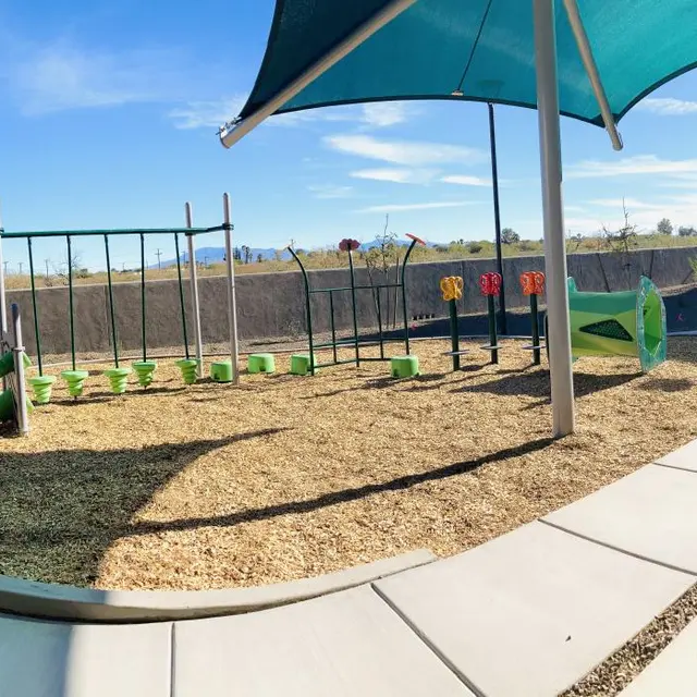 Children's Playground Area A playground area featuring green equipment, swings, and a large shade structure, surrounded by gravel and a paved pathway.