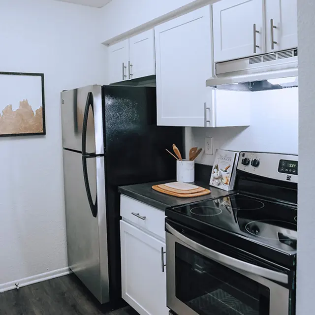 Kitchen with white cabinets, white walls and stainless steel appliances on hardwood-style flooring.