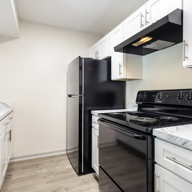 A modern kitchen featuring white cabinets, a black refrigerator, a black oven, and marble countertops.