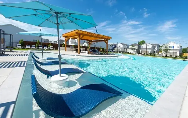 Sunny Poolside Retreat A sunny pool area featuring lounge chairs with umbrellas, a social pavilion, and clear blue water.