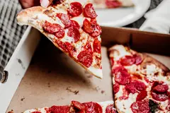 person grabbing a slice of pepperoni pizza from the entire pie