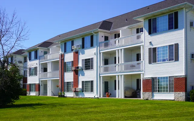Modern apartment building with white siding, red accents, balconies, and a green lawn.