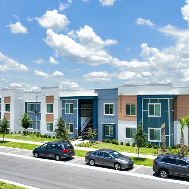 A modern apartment complex with a contemporary design, featuring multiple units, green lawns, and parked cars.