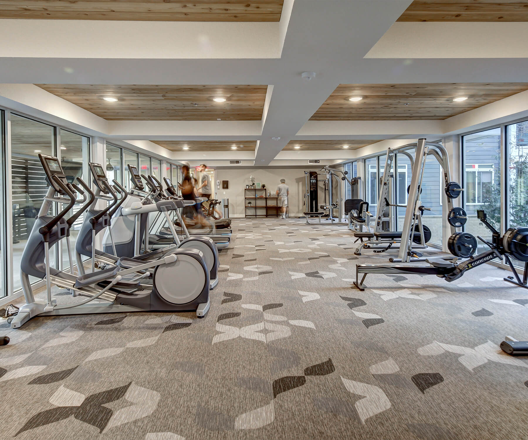 Fitness center furnished with various exercise equipment, carpet flooring, and huge windows for natural lighting.
