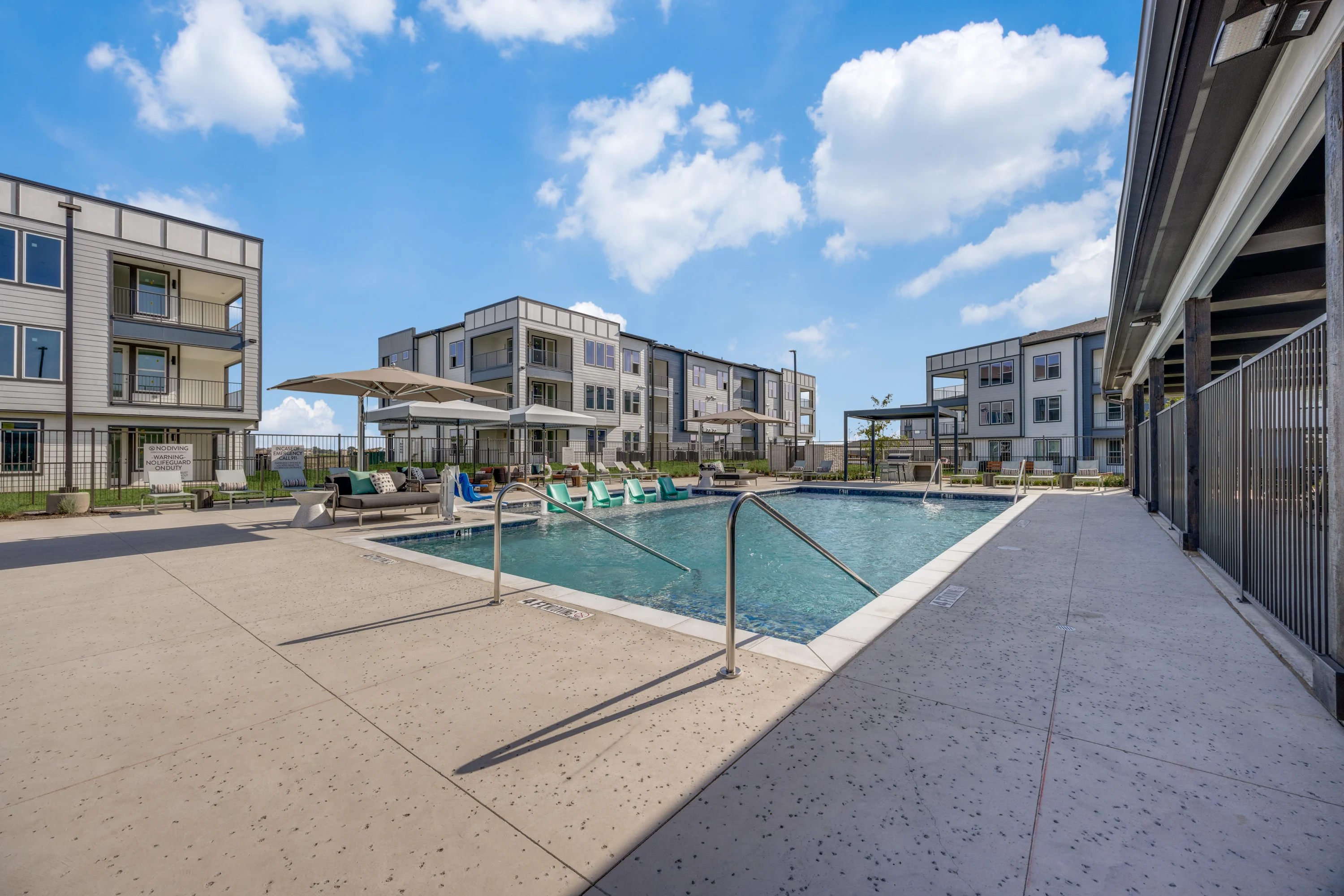 Modern Apartment Complex with Pool A modern apartment complex with a swimming pool and lounge chairs under shaded umbrellas.