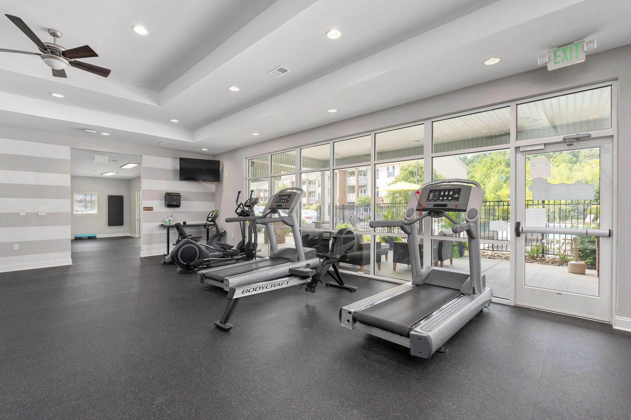 Modern Gym Space in Apartment Community A modern gym interior featuring cardio equipment including treadmills and stationary bikes, with large windows allowing natural light to enter.