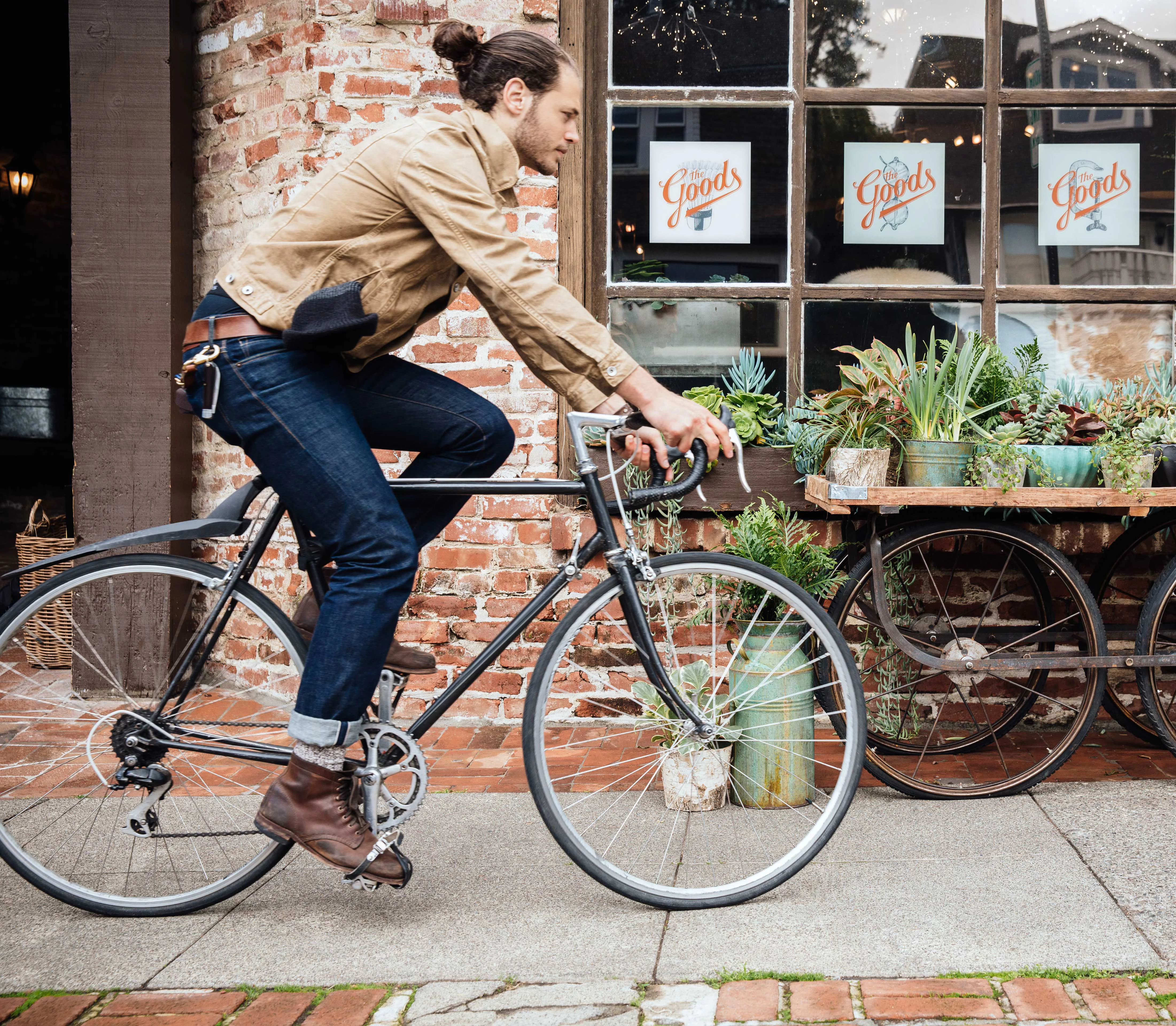 A man riding a bicycle past a brick building with large windows displaying plants and signage.