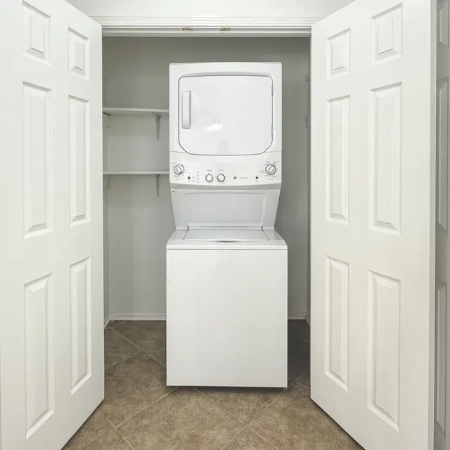 A small laundry room featuring a stacked washer and dryer unit between two closed white doors.