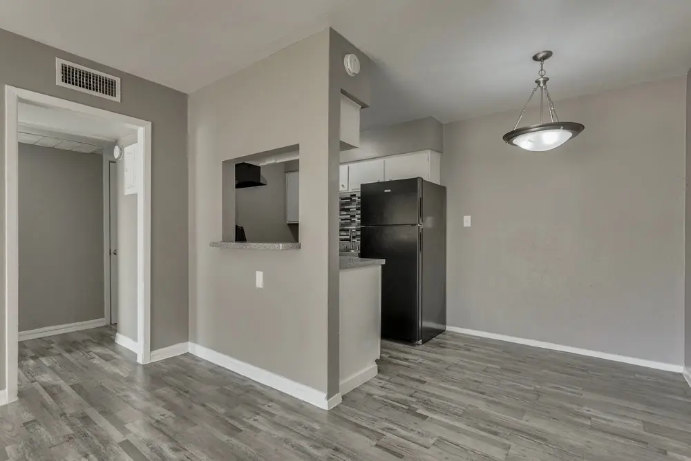 A modern apartment interior featuring an open layout with gray walls, a kitchen area with a black fridge, and wood-style flooring.
