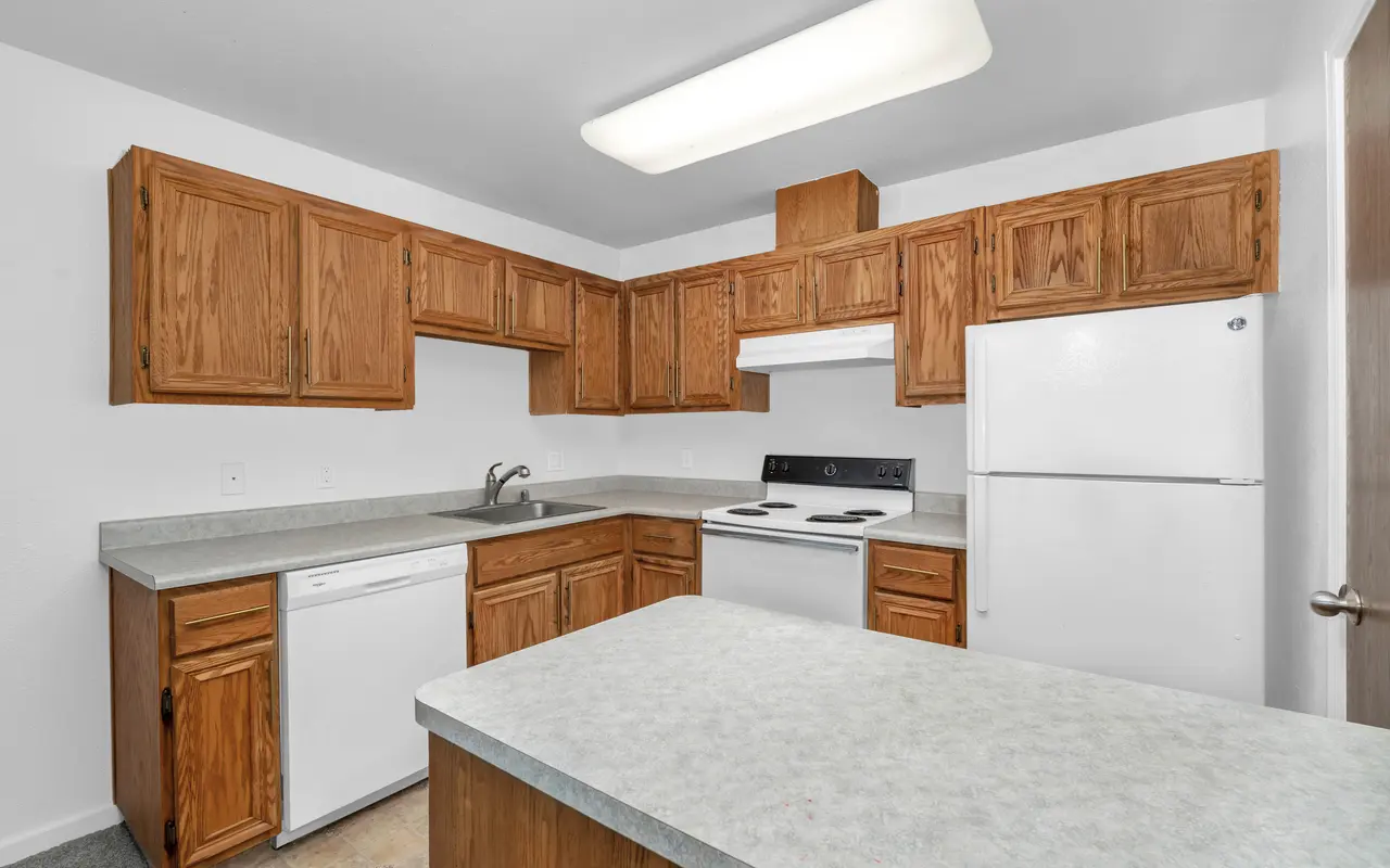 A modern kitchen featuring wooden cabinets, white appliances, and a light gray countertop.