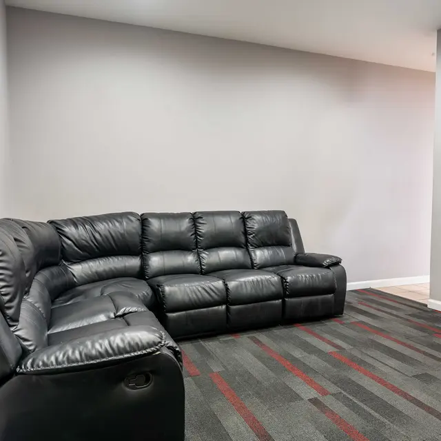 A modern black leather sectional sofa placed in a room with gray walls and striped carpet.