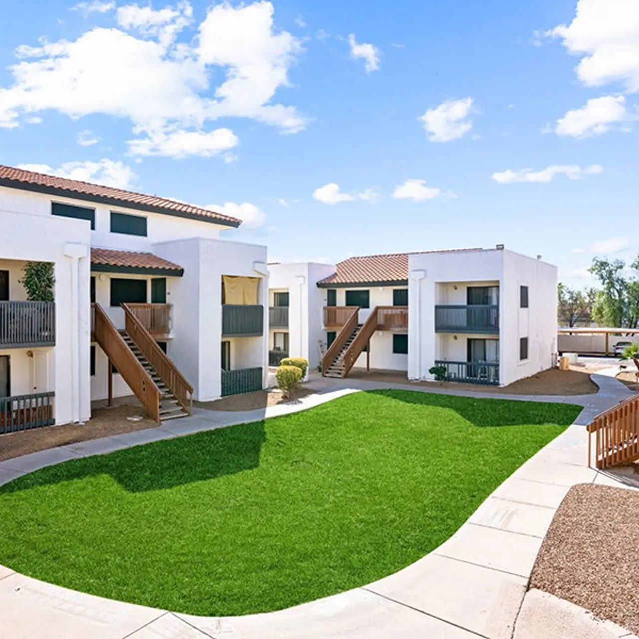 A sunny view of an apartment complex featuring white buildings, green grass, and blue skies.