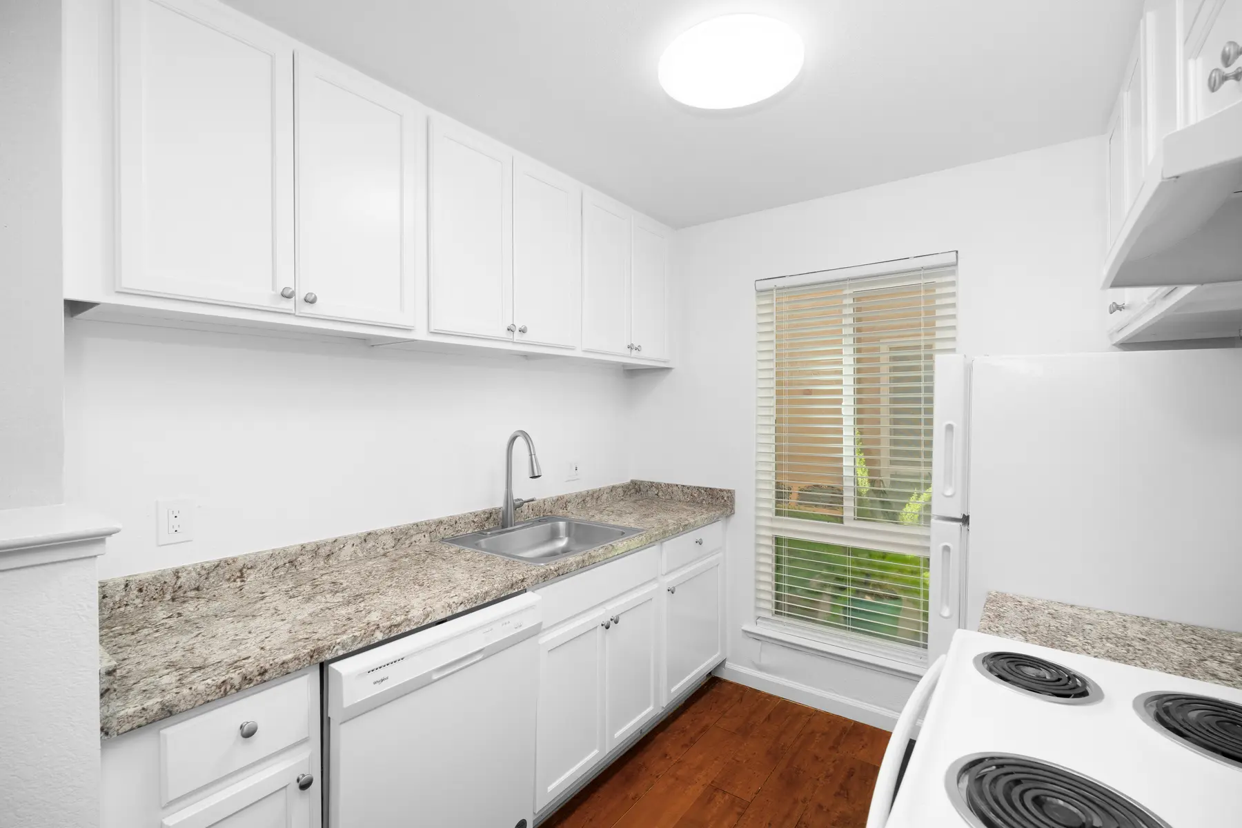 A modern kitchen with white cabinets, a granite countertop, a sink, and a window with blinds.