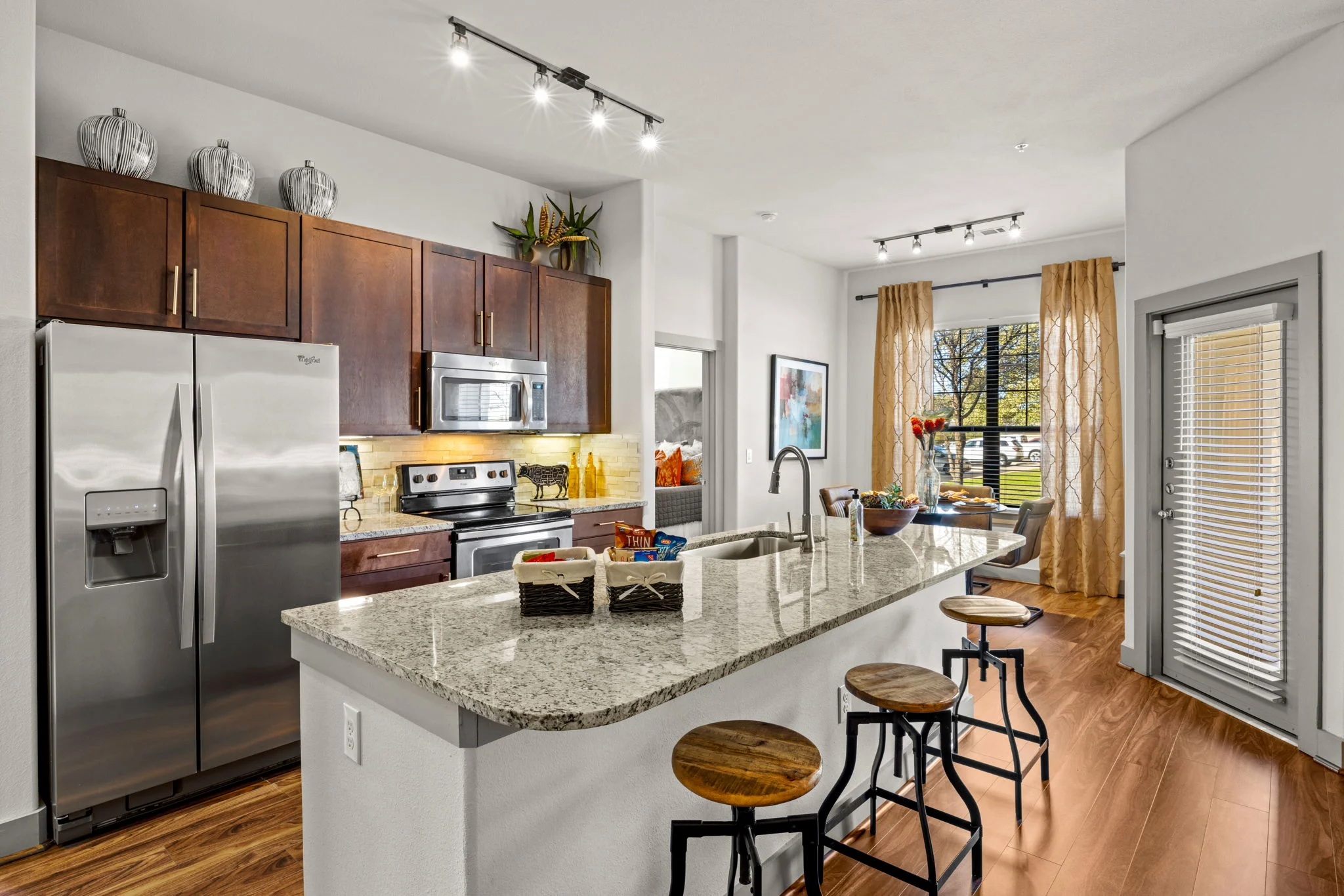 A modern kitchen with stainless steel appliances and a living area featuring large windows and decorative curtains.