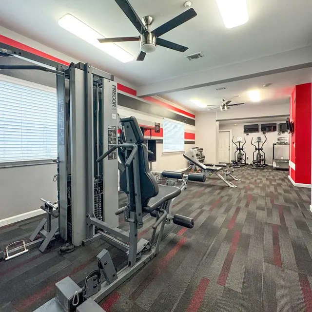 A modern gym interior with workout equipment including weight machines and cardio machines, featuring a stylish color scheme with red, gray, and black accents.