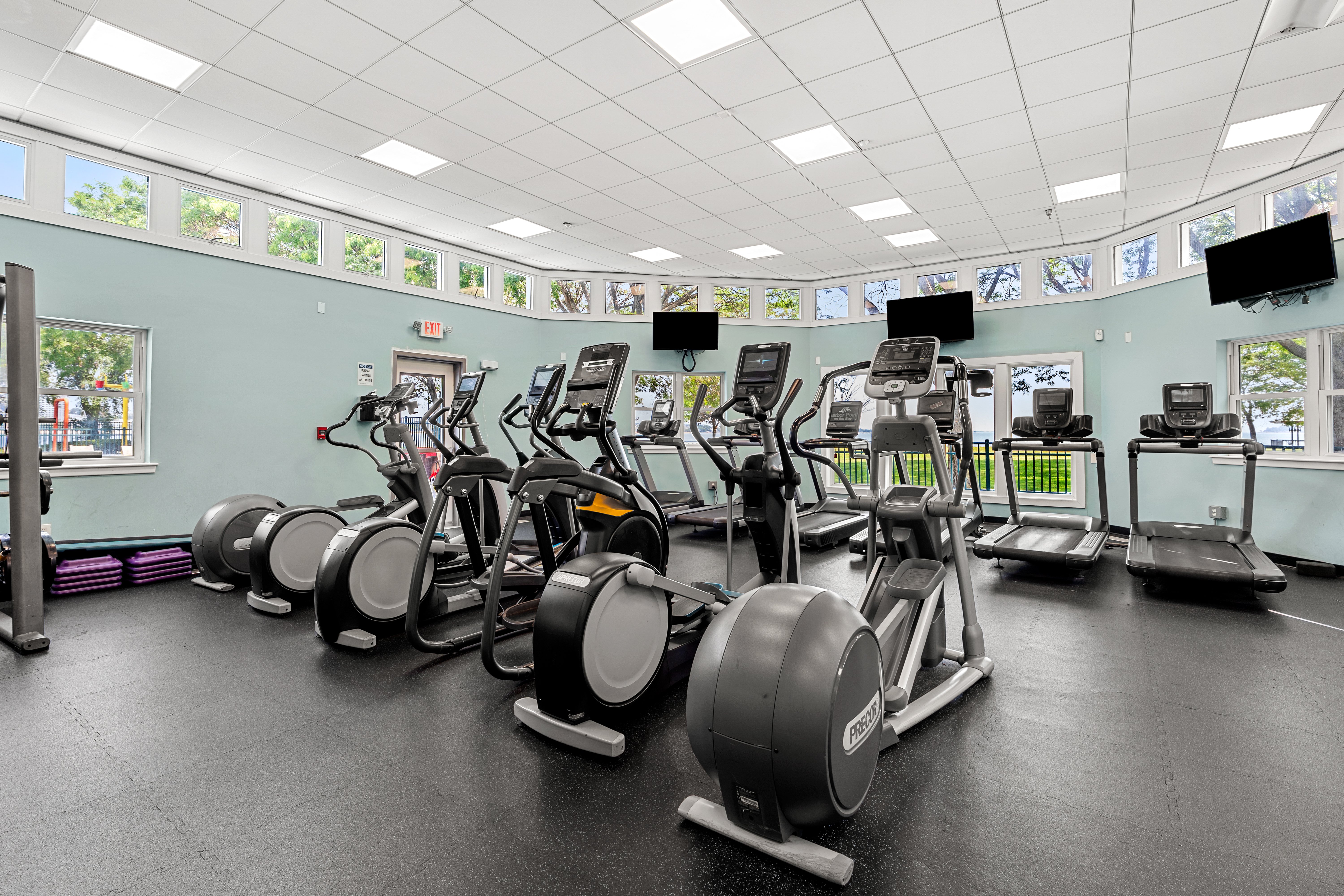 Interior of a Fitness Gym Interior view of a fitness gym featuring various cardio machines, including ellipticals and treadmills, with large windows allowing natural light to enter.