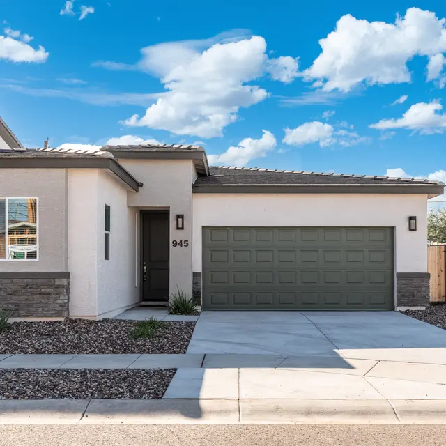 A modern single-story house with a light-colored exterior and a green garage door, surrounded by gravel landscaping and blue skies with fluffy clouds.