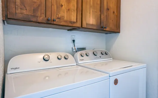 Laundry Room with Whirlpool Appliances A laundry room with a washer and dryer side by side, featuring wooden cabinets above.