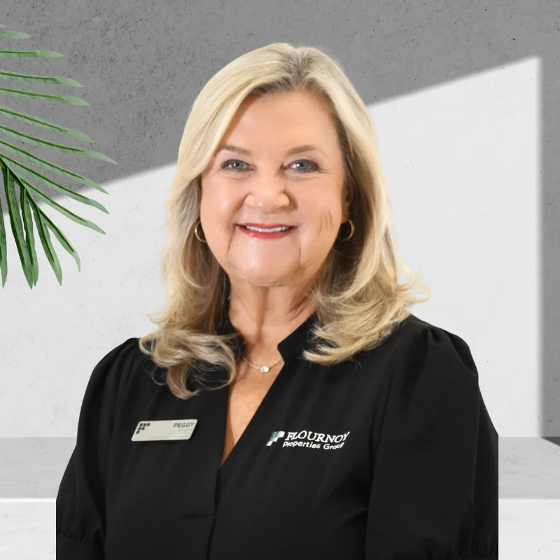 Professional Portrait A smiling woman in a black shirt with a name badge, standing in front of a simple background with a green plant.