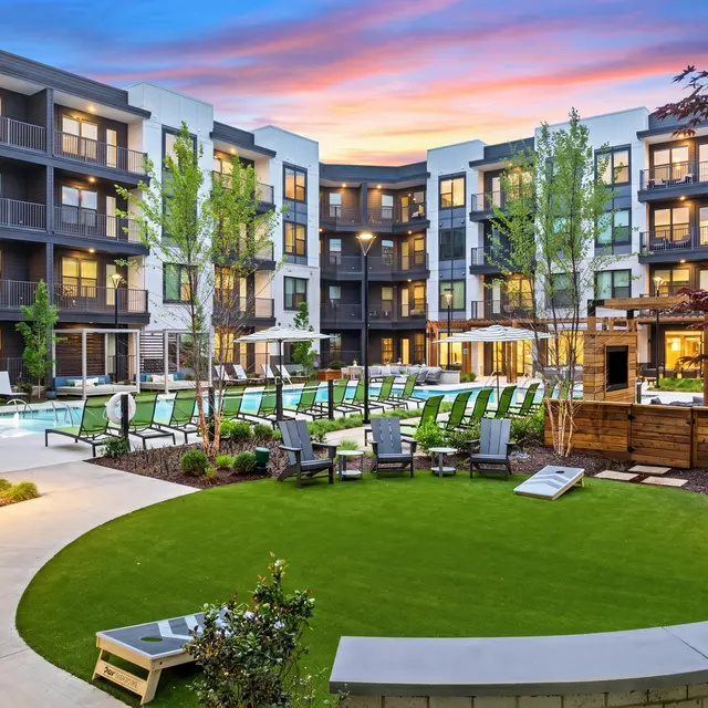 Serene Apartment Community with Pool A beautifully designed apartment complex featuring a community pool area with lounge chairs, surrounded by greenery and trees at sunset.
