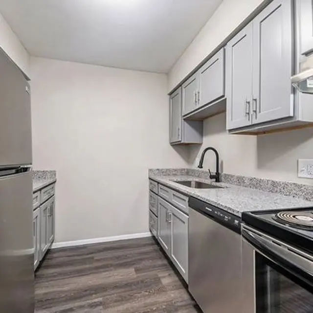 A modern kitchen featuring stainless steel appliances, gray cabinetry, and granite countertops. The space is well-lit and has a clean design with wooden flooring.
