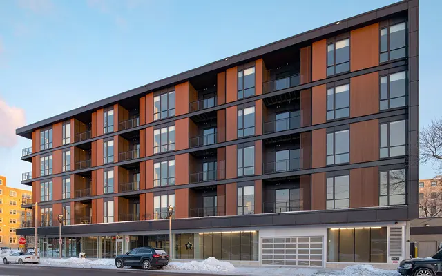 Contemporary Apartment Building in Winter A contemporary four-story apartment building with wooden and glass exterior, featuring balconies and large windows, located in a snowy environment.
