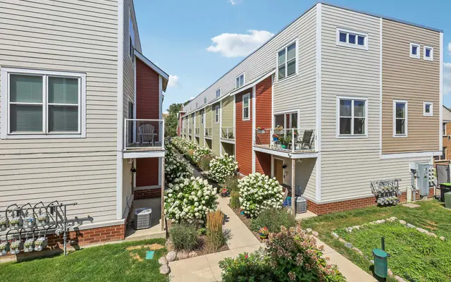 A view of a residential housing complex featuring two-story buildings with a mix of siding colors, surrounded by green grass and flower beds.