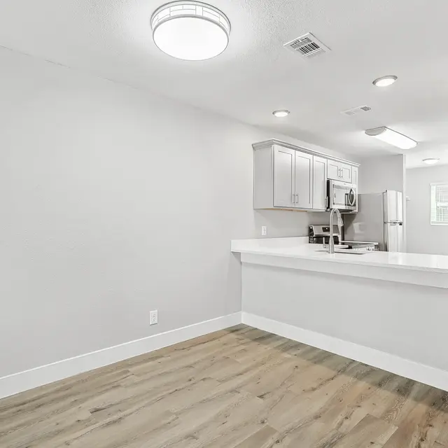 A modern kitchen space featuring light-colored cabinets and a spacious countertop, with wooden flooring and bright lighting.