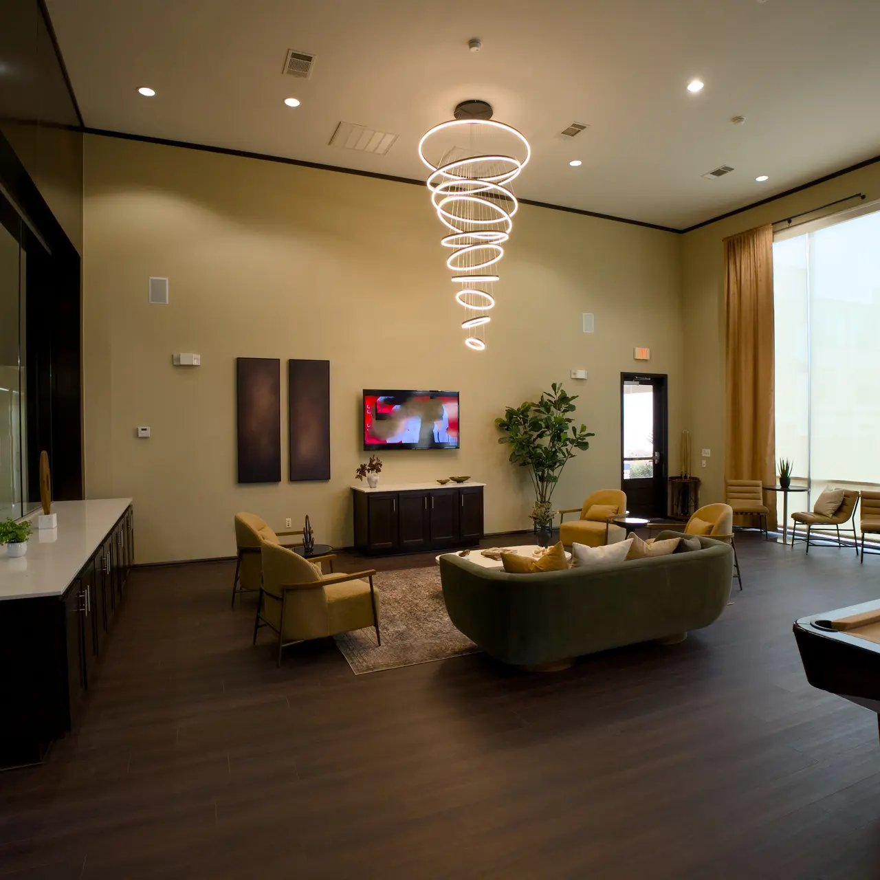 A stylish modern lounge area featuring a green sofa, pool table, large windows with natural light, and contemporary decor.