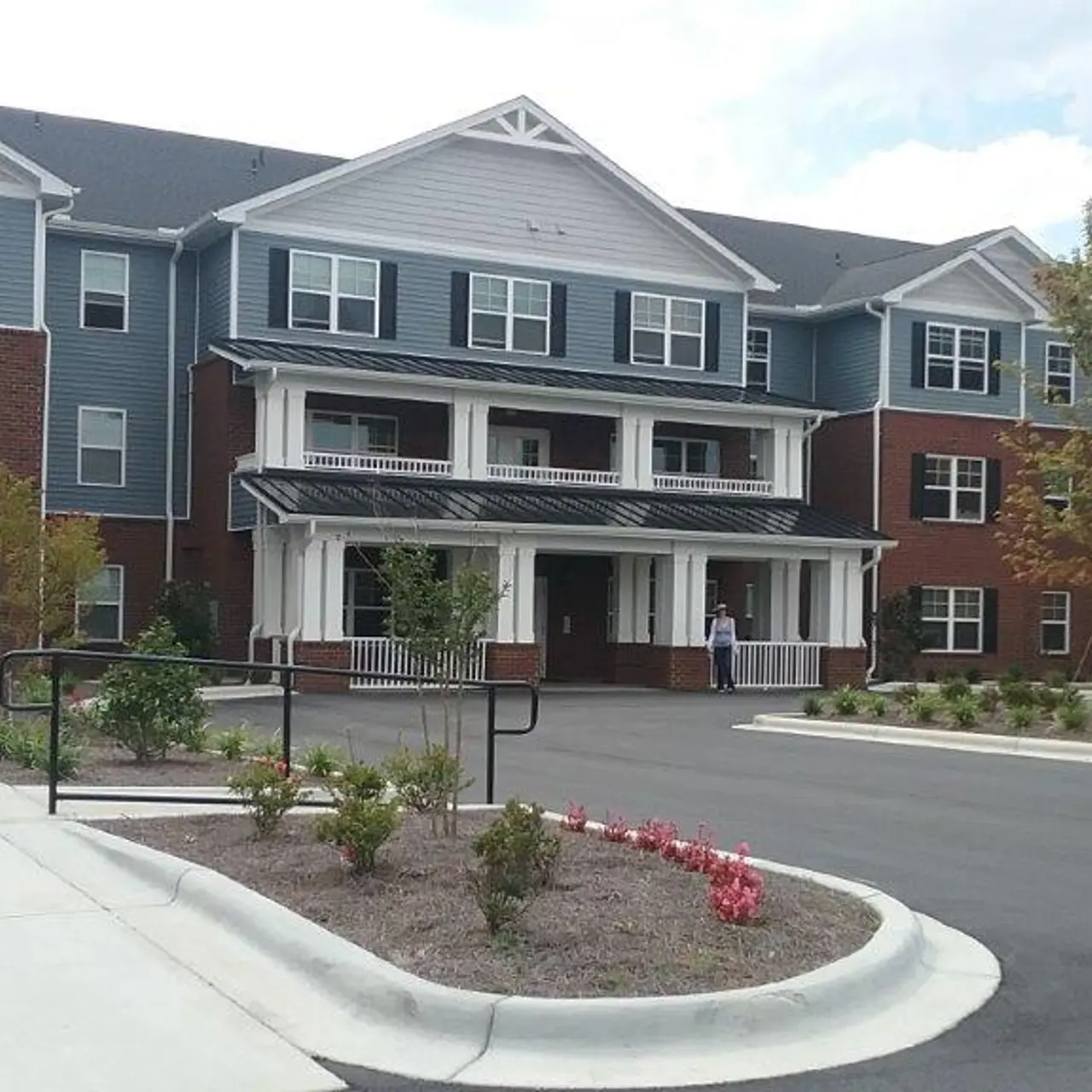 A modern apartment building featuring a combination of brick and blue siding, with a welcoming entrance and landscaped surroundings.