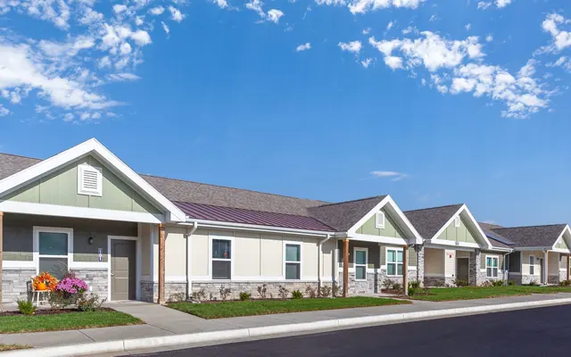 Modern Housing Complex A modern housing complex featuring several single-story houses with gabled roofs, green and beige siding, and neatly landscaped yards under a clear blue sky.