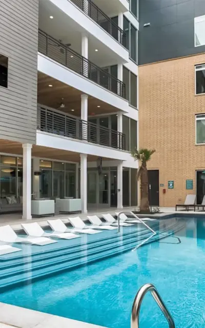 Outdoor resort-style swimming pool at 120 Ninth Street Apartments, surrounded by modern lounge chairs and shaded by table umbrellas.