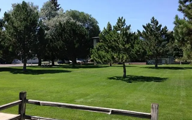 Exterior view of Twin Cedars Apartments in Helena, Montana, with lush green lawn and mature shade trees