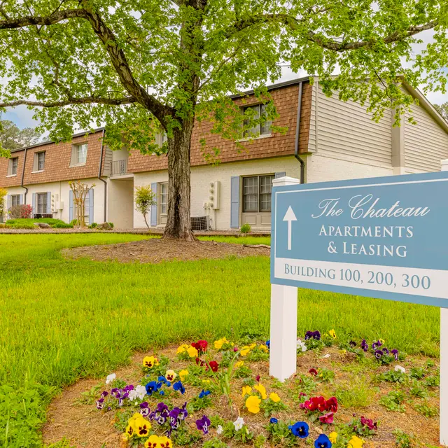A residential apartment complex sign in front of well-maintained buildings and colorful flower beds.