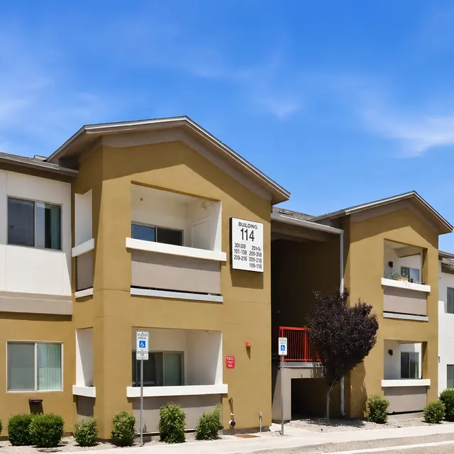 Multi-Unit Apartment Building Exterior view of a multi-unit apartment building with tan and white walls and green landscaping.