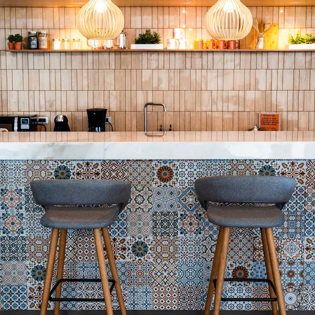 Two gray bar stools are positioned in front of a marble countertop, complemented by decorative tiled walls and modern pendant lights above.