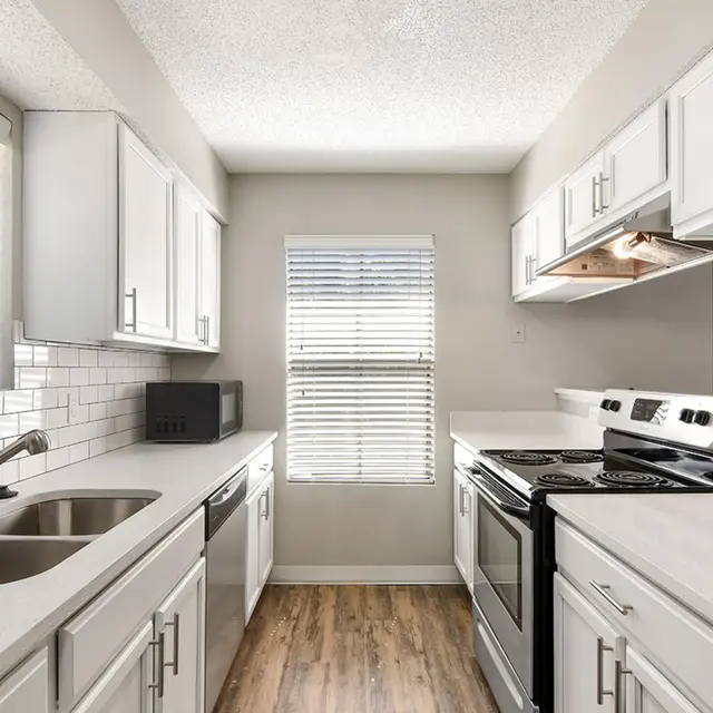 Venice Park kitchen facing a window with a sink and white countertops across from a stainless steel oven.