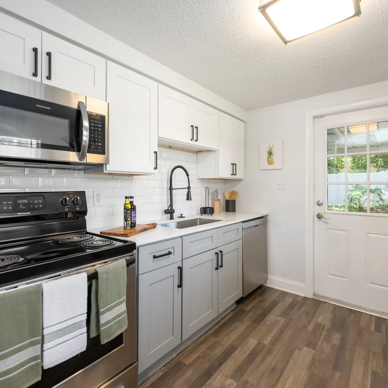 A modern kitchen featuring stainless steel appliances, including a microwave and stove, white cabinetry, a sink with a black faucet, and a door leading to an outdoor area.