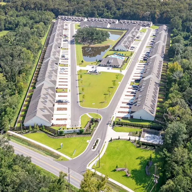 Aerial View of Residential Complex Aerial view of a residential complex surrounded by greenery, featuring a central road and parking spaces.