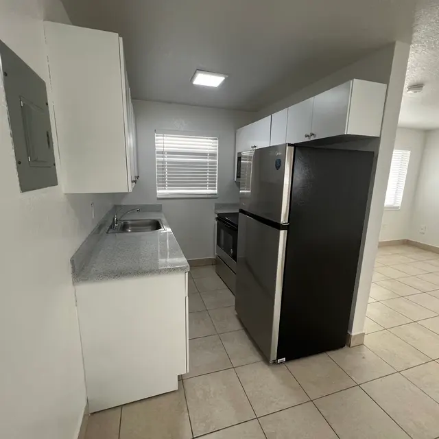 Modern kitchen with white cabinets, stainless steel appliances, and tile flooring, brightly lit by a ceiling fixture.