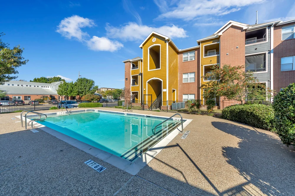 Apartment Pool Area Brightly lit apartment pool area with clear water and surrounding foliage.