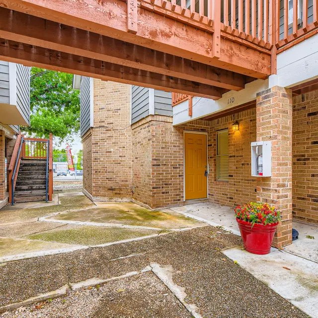 View of an entrance area in an apartment complex featuring brick walls and a wooden walkway overhead.
