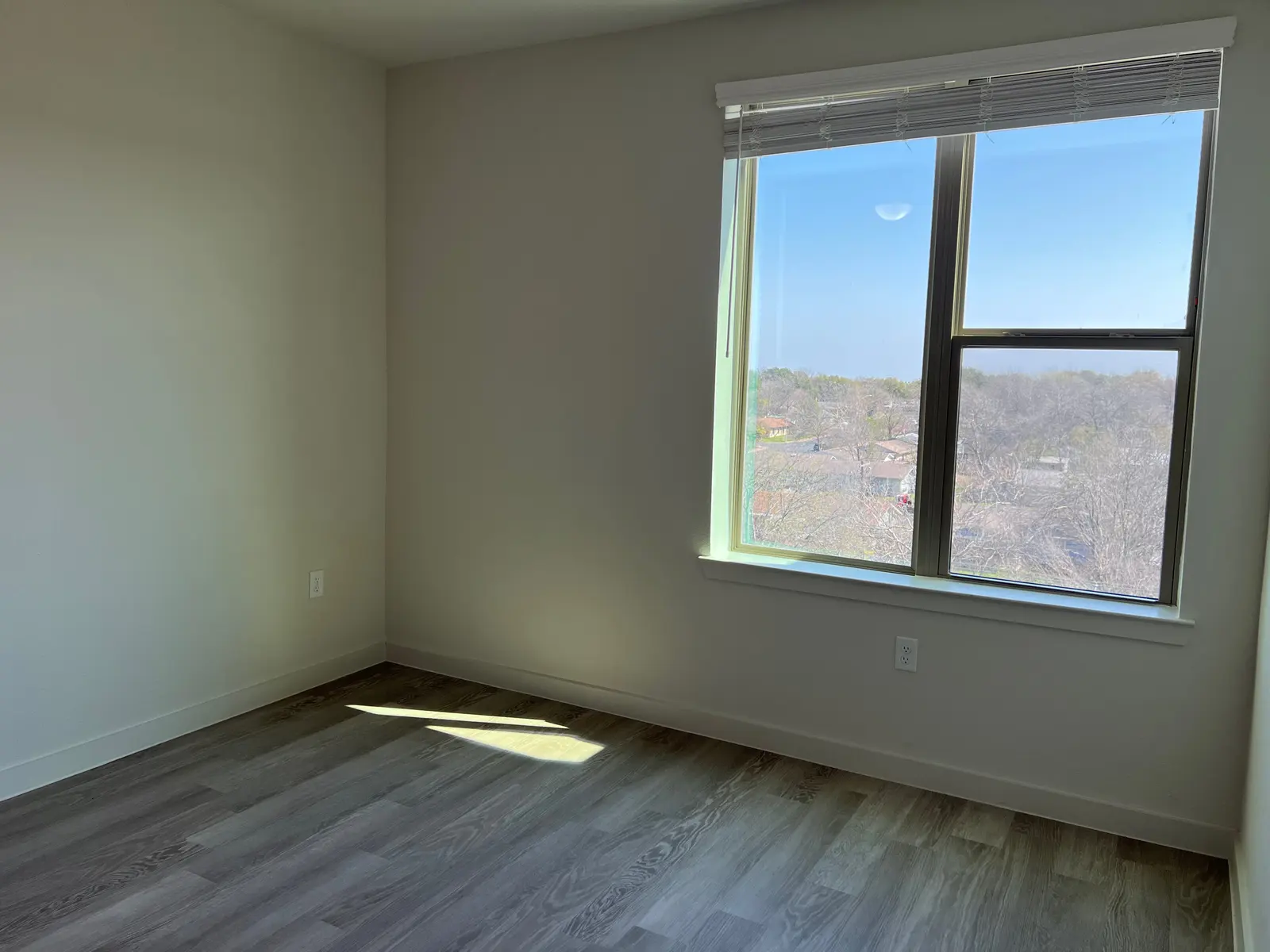 An empty room with a large window, featuring natural light and a view of the outdoors.